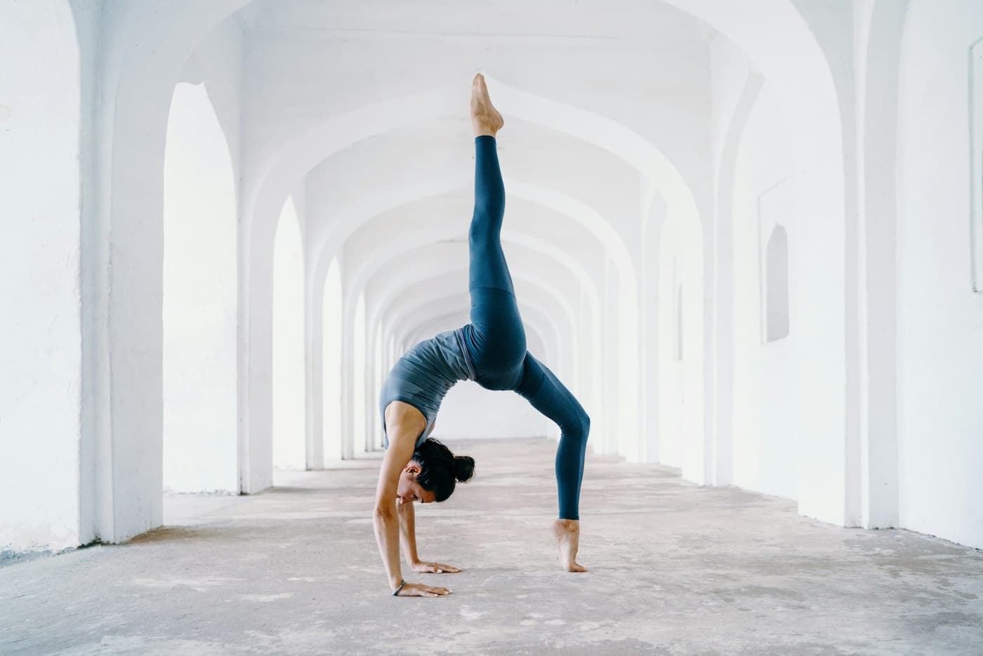 Woman in a one-legged backbend beneath white stone arches