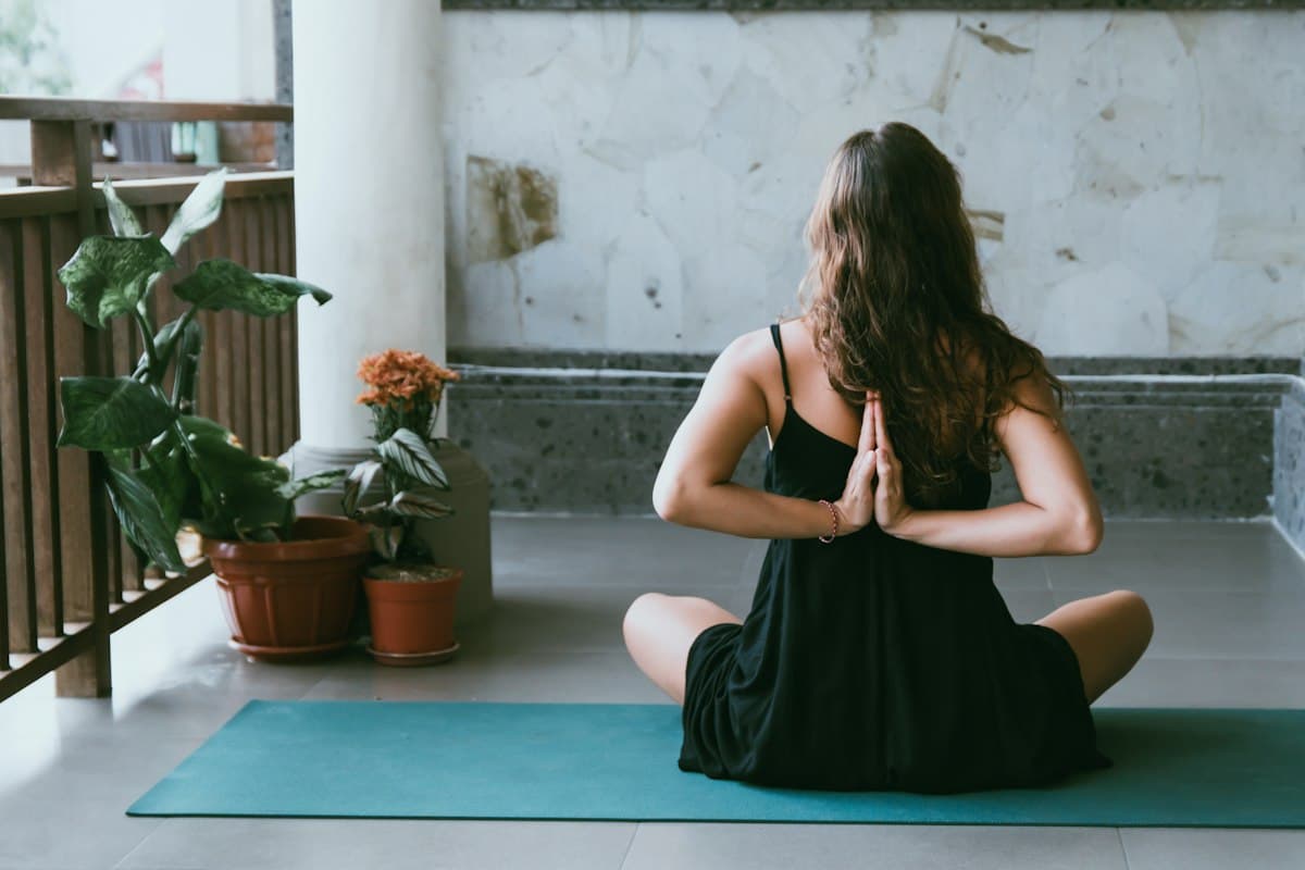 Teacher seated in prayer pose on a balcony surrounded by plants