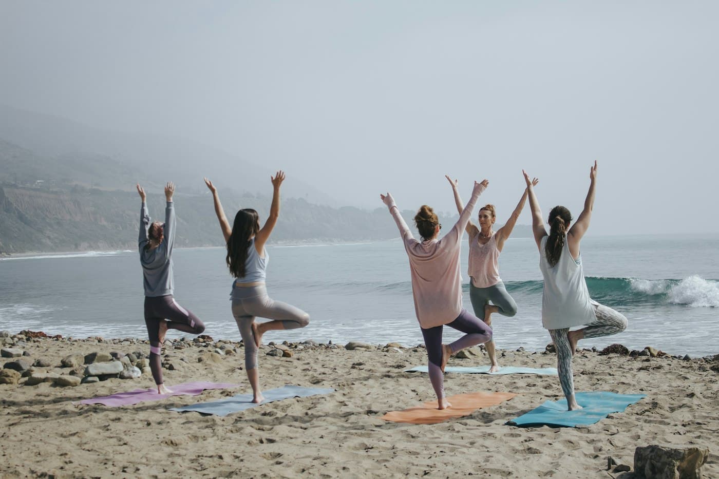 Students standing in tree pose on a misty beach