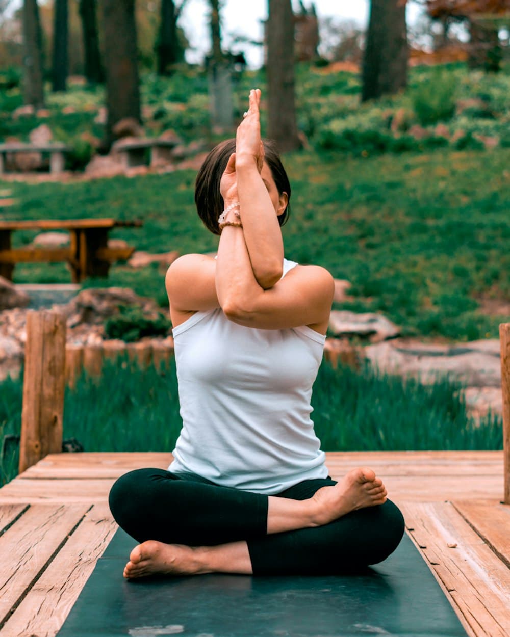 Woman in eagle arms pose on a garden deck