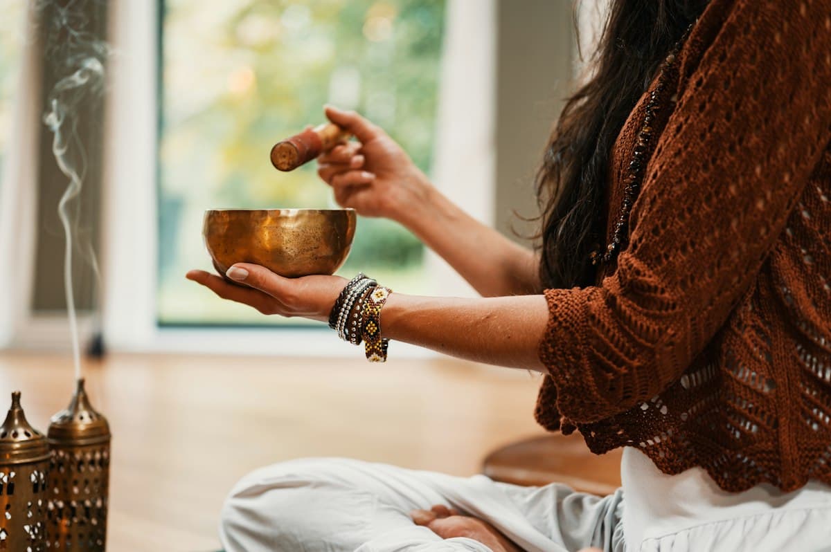 Hands holding a brass singing bowl beside incense