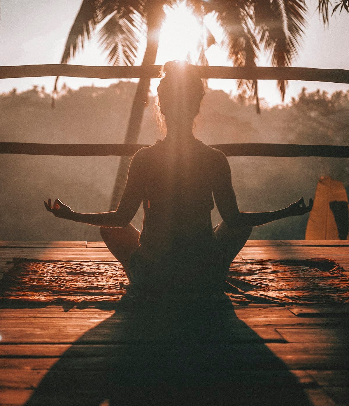 Person meditating at sunrise on a wooden deck under palm trees