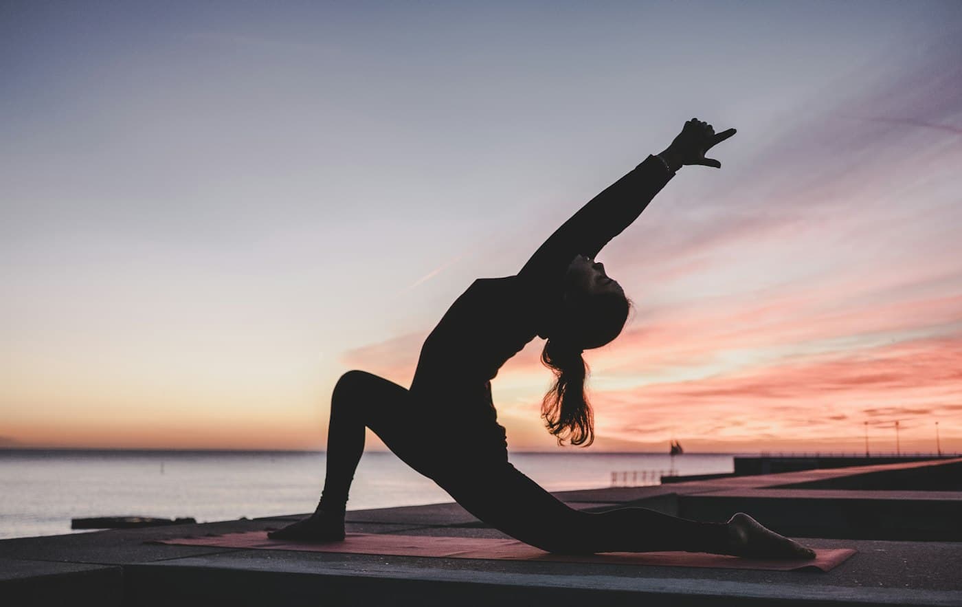 Woman in a low crescent lunge silhouetted against a pink sunset